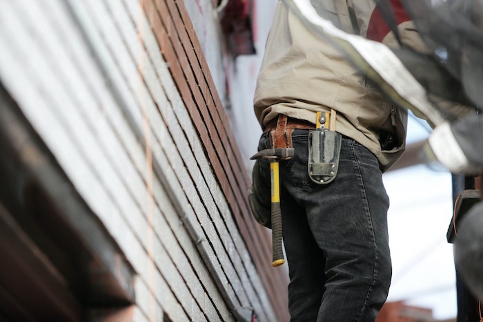 contractor working on a project near the side of a building and has a tool belt with a hammer and knife visible